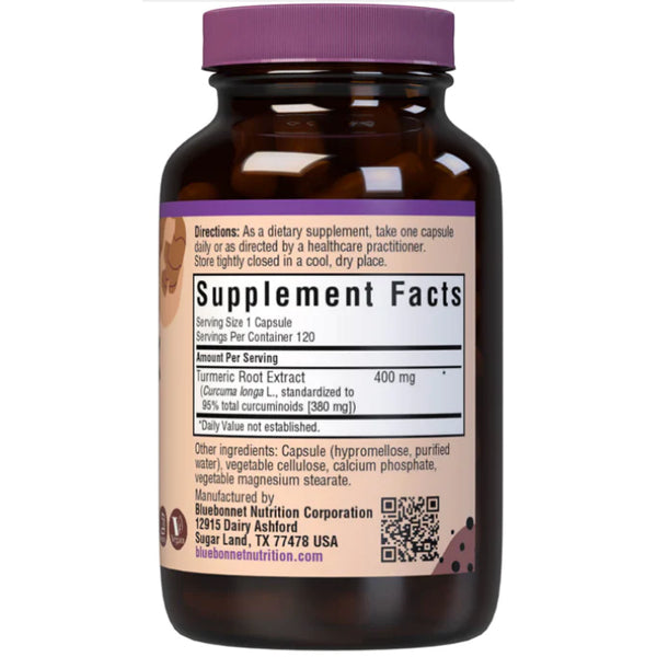A hand holding turmeric extract capsules against a backdrop of fresh turmeric roots.